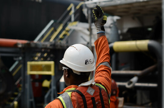 The bosun is giving hand signals to the crane operator during deck cargo operations between the offshore support vessel and the FPSO. These operations are taking place at the oilfield