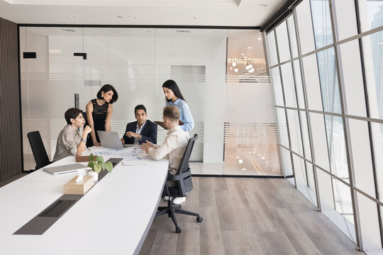 Five diverse teammates solve business-related matters during briefing in contemporary meeting room, listening opinion, idea or point of young male colleague, looking interested, engaged in teamwork