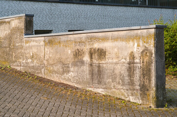 Low concrete wall protecting building with grey bricks and paving stones