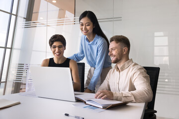 Smiling diverse employees working together, reviewing financial spreadsheets or budgets for project, discussing report, researching, learning new business AI tools or software application using laptop