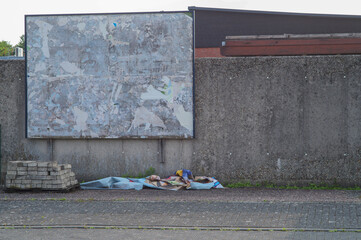 Empty billboard showing decaying posters and discarded materials on sidewalk