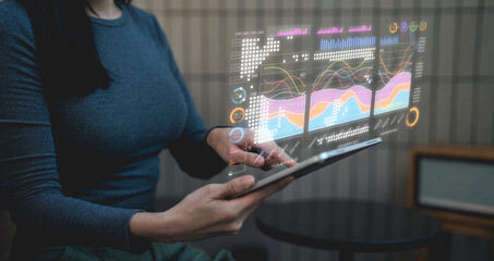 A person interacts with a futuristic transparent digital interface displaying colorful graphs and data visualizations above a tablet.