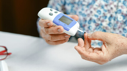 Blood glucose meter diabetes test elderly hand pricking finger home health care monitoring sugar level close up medical device chronic illness daily routine