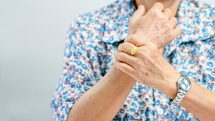Elderly person wearing floral shirt, holding their wrist with one hand, gold ring and silver...