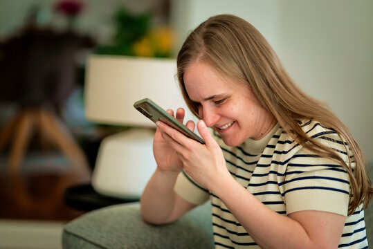 A visually impaired woman sitting on the sofa and using her cell phone