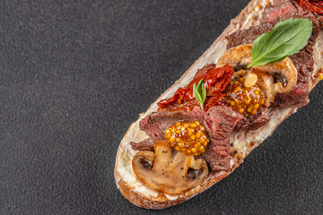 Gourmet open-faced sandwich with seared beef, mushrooms, sun-dried tomatoes, mustard seeds, and fresh basil on crusty bread