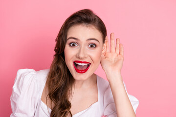 Excited young woman wearing a stylish white dress, gesturing with her hand near ear on vibrant pink...