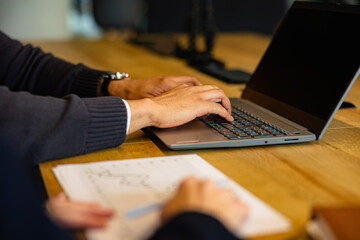 Businessman working on a laptop, analyzing financial data while a colleague diligently taking notes during a strategic office meeting