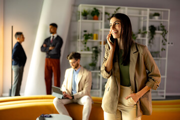 Businesswoman smiling and talking on phone while colleagues working in background at the office