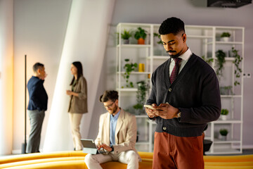Businessman using smartphone in modern office with colleagues working on tablet and talking in background