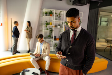 Businessman using smartphone in modern office with colleagues working in background, concept of technology and business