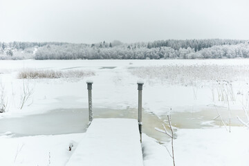 a frozen lake and a forest in frost around the lake, winter fairy tale in the forest, snow-covered tree branches, large flakes of snow are slowly falling, nobody