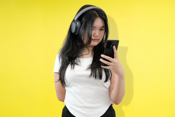 Obraz premium young asian woman seriously looking at phone with headphone in yellow studio background
