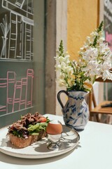 Sandwich with meat, egg and with freshly greens. Crop delicious breakfast served on wooden table in sunny outdoor cafe. Part of a series.