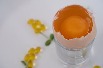A top-down perspective of a cracked eggshell filled with a raw egg yolk, surrounded by golden vitamin D capsules shaped like flowers.