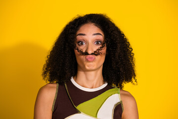 Playful young woman with curly hair making funny face against vibrant yellow background