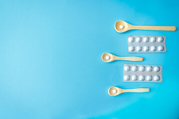 Flat lay with pills in wooden spoons and blister packs on blue background. Modern approach to medicine, nutrition, and natural supplement care