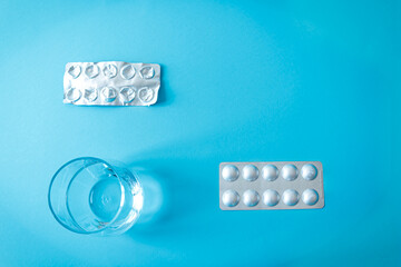 Glass of water and blister packs of pills, some empty. Minimalist composition about daily...