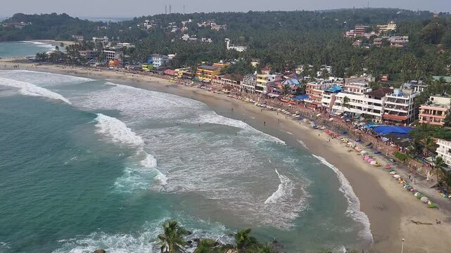 Stunning aerial view of Kovalam Beach, where the turquoise ocean gently kisses the golden coastline, surrounded by charming seaside buildings and lush green trees swaying in the breeze