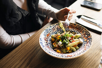 Woman eating vegetable salad with feta cheese in a restaurant, close-up.