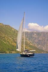 Beautiful Mediterranean landscape on sunny summer day. Sailboat with white sail on water.  Vacations, recreation, sport concepts. Montenegro, Adriatic Sea, Bay of Kotor