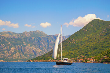 Beautiful sunny Mediterranean landscape. Montenegro, Bay of Kotor.  Sailboat with white sail on water.  Recreation, sport concepts