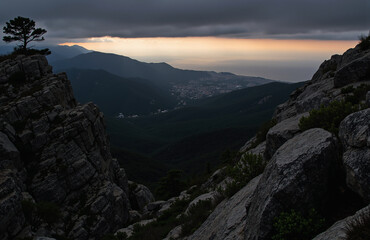 Naklejka premium Moody mountainous landscape with lone tree, rocky foreground, sunset.