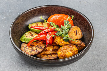 Assorted grilled vegetables including zucchini, eggplant, pepper, corn, and tomato served in a rustic bowl.