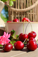  A vibrant close-up of ripe red cherries and a blooming pink rose on a wooden table in the sun. The composition highlights freshness, summer, and natural beauty.