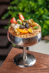 Luxury tiramisu in a silver coupe topped with berries, pistachios, mint, and edible gold
