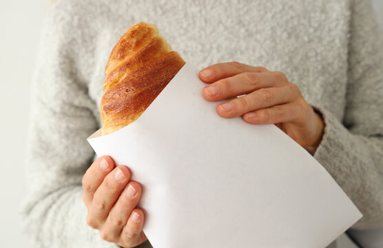 Woman's hand hold a fresh whole croissant. Closeup on croissants with butter in french pastry shop.