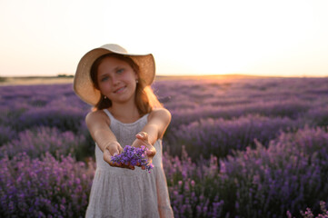 Little girl in summer dress and hat holding lavender bouquet in blooming lavender field. Romantic...