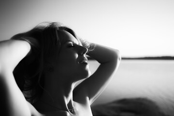 Black and white portrait of a sexy young woman in close-up against a seascape background. The...