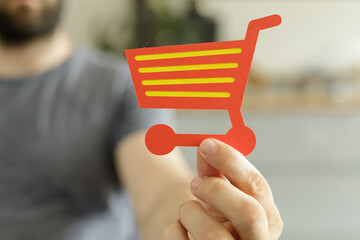 Image of a person holding a red paper shopping cart icon.  Perfect for e-commerce, online shopping,...