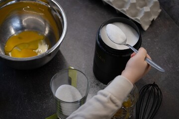Small hand measuring sugar for baking in kitchen with eggs and mixing tools