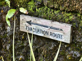 A weathered wooden Evacuation Route Sign and a pointing arrow on a mossy rock wall