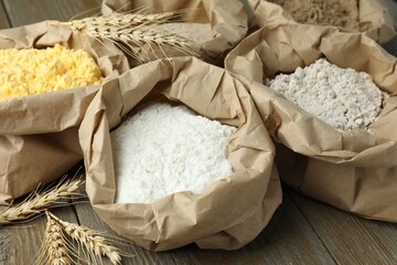 Different types of flour in paper bags on wooden table, closeup