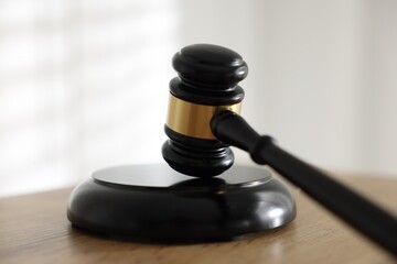 Judge's gavel on wooden table against light background, closeup