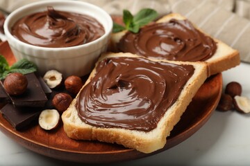 Toasts with chocolate hazelnut spread, nuts, pieces of chocolate and mint on white marble table,...