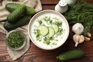 Tasty cucumber soup in bowl and ingredients on wooden table, flat lay