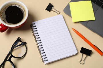 Notebook, pen, sticky note, binder clips, glasses, coffee and laptop on beige background, above view