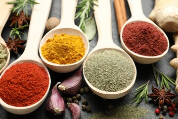 Different aromatic spices in spoons on black table, closeup