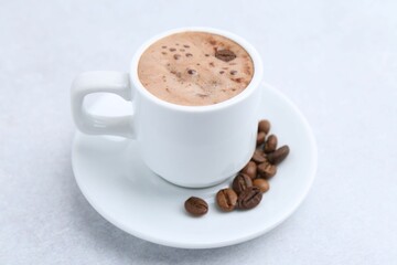 Aromatic coffee in cup, beans and saucer on light table, closeup