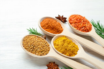 Different aromatic spices in spoons on white wooden table, closeup