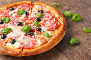 Tasty pizza with salami, cheese, basil and olives on wooden table, closeup
