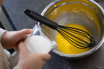 Child pouring sugar into egg yolk mixture with focus on whisk