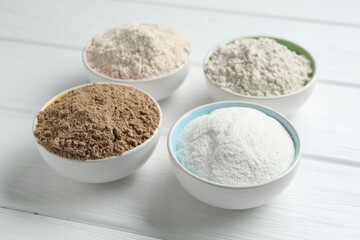 Different types of flour in bowls on white wooden table, closeup