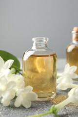 Bottles of essential oil and jasmine flowers on grey table, closeup