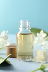 Bottle of essential oil and jasmine flowers on light blue background, closeup