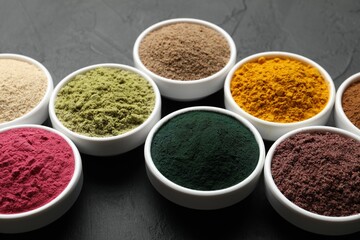 Different superfood powders in bowls on dark textured table, closeup
